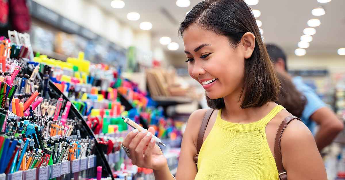 seorang perempuan megenakan tanktop kuning berada di toko alat tulis sambil memegang pulpen bangkit perkasa sukses distributor ATK kantor terlengkap seindonesia